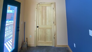 A hallway with a wooden door, a broom leaning against the wall, and a blue wall. - Taborton Harvest Timber Trails
Unique cabin experience (Sand Lake)
