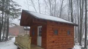 A small wooden cabin with a porch and a door, surrounded by snow and trees. - Taborton Harvest Timber Trails
Unique cabin experience (Sand Lake)