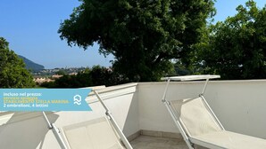 Eine Dachterrasse mit zwei Liegestühlen, Blick auf eine Stadt und einem klaren Himmel.