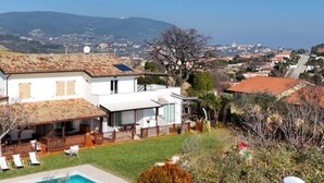 Ein zweistöckiges Haus mit Pool, umzäunter Terrasse und Blick auf die umliegende Landschaft.