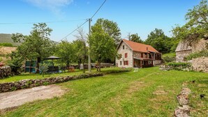 A rustic stone house with a red-tiled roof, surrounded by a grassy yard and trees.