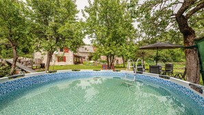An outdoor swimming pool surrounded by trees and stone buildings.