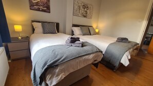 A double bed with a striped blanket and a pillow, a nightstand with a lamp, and a wall with two paintings. - Waterworks En Suite Rooms with Private Living Room (Belfast)
