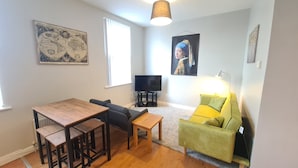 A living room with a wooden dining table, a sofa, a TV on a stand, and a lamp. - Waterworks En Suite Rooms with Private Living Room (Belfast)
