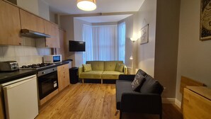 A compact living space with a kitchenette, a sofa, and a TV mounted on the wall. - Waterworks En Suite Rooms with Private Living Room (Belfast)