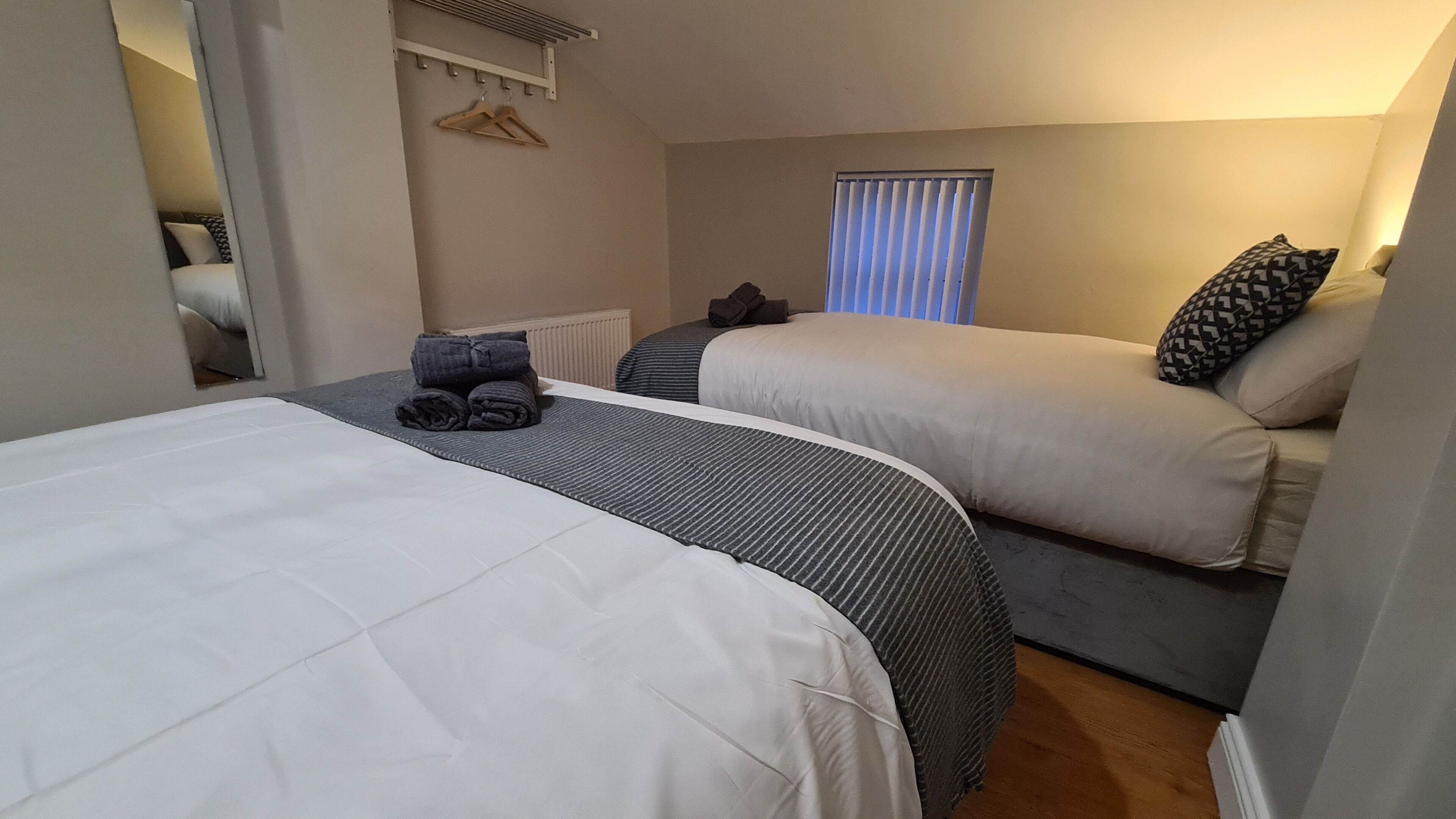 A hotel room with two beds, a radiator, a window with blinds, and a coat rack with hangers.