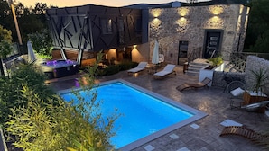 A swimming pool with lounge chairs, a hot tub, and a stone building with outdoor lighting. - Luxurious home in Biorine (Biorine)