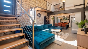 A modern living space with a staircase, a blue sofa, a dining area, and a kitchen. - Luxurious home in Biorine (Biorine)
