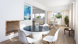 A modern dining area with a glass table, white chairs, and a brick fireplace. - Home2Book Exquisite Apt&Terrace, Puerto de la Cruz (Puerto de la Cruz)