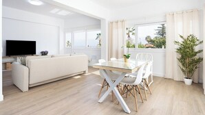 A modern living room with a sofa, a TV, a dining table with chairs, and a large window with curtains. - Home2Book Exquisite Apt&Terrace, Puerto de la Cruz (Puerto de la Cruz)