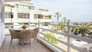 A balcony with wicker chairs and a table, overlooking a street with palm trees and parked cars. - Home2Book Exquisite Apt&Terrace, Puerto de la Cruz (Puerto de la Cruz)