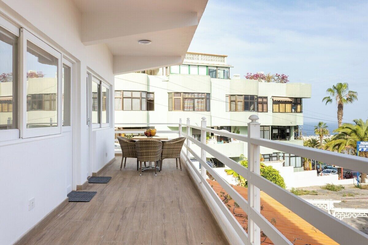 Un balcon avec une table et des chaises, donnant sur un quartier résidentiel avec des immeubles et un ciel dégagé.