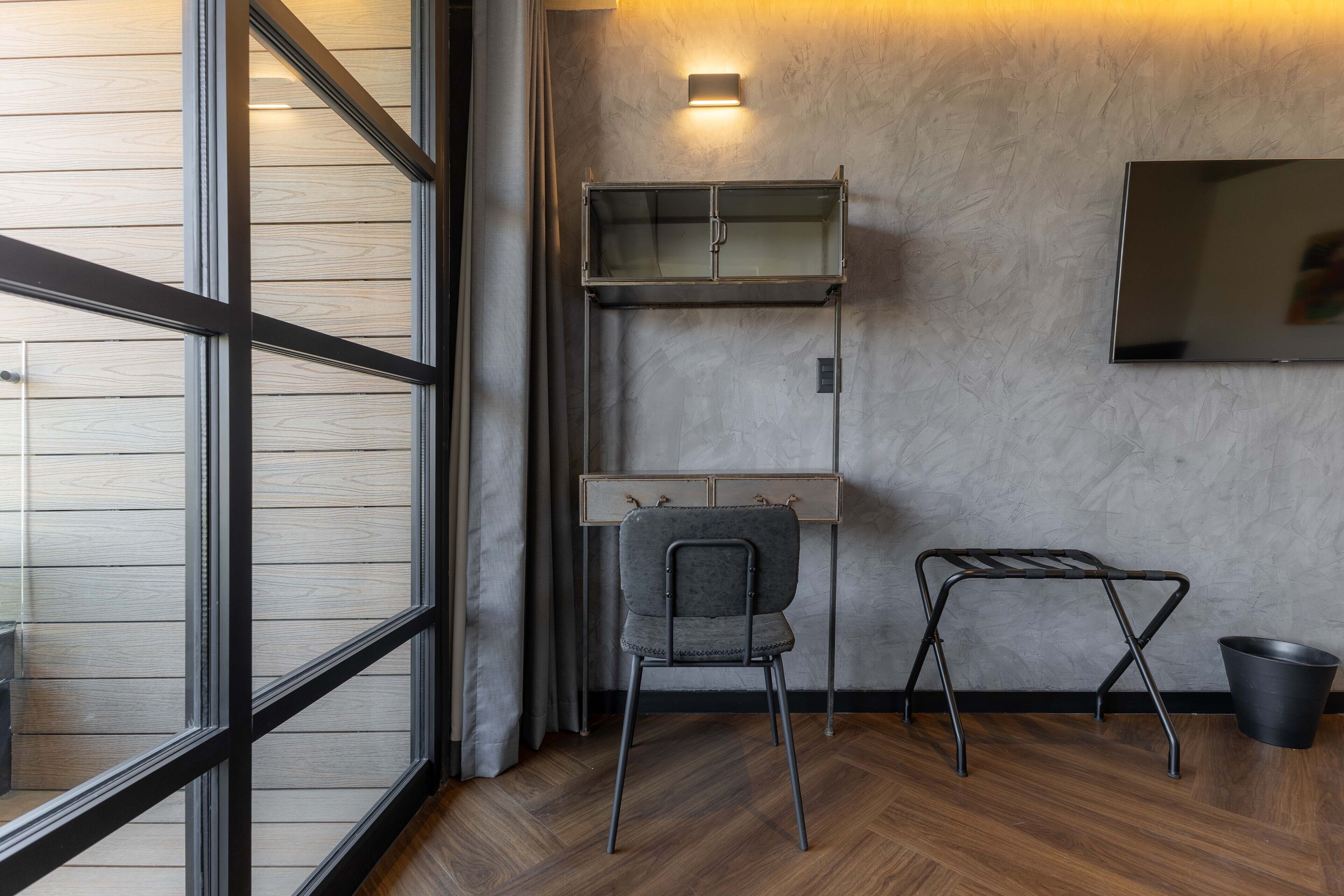 Una habitación con piso de madera, una silla gris, un estante metálico y un cubo negro.