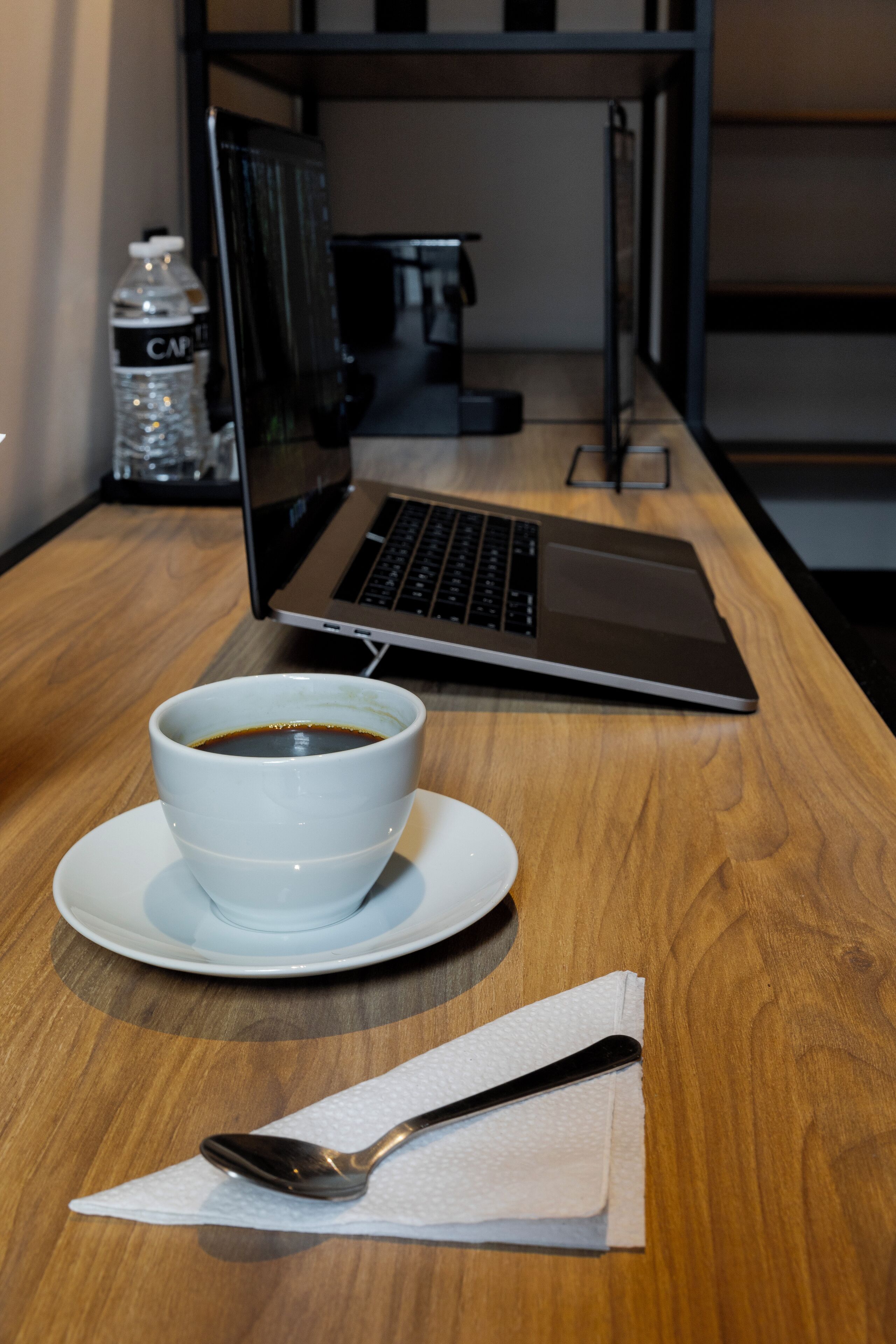Ein Laptop auf einem Holztisch mit einer Kaffeetasse und einem Löffel auf einer Serviette.