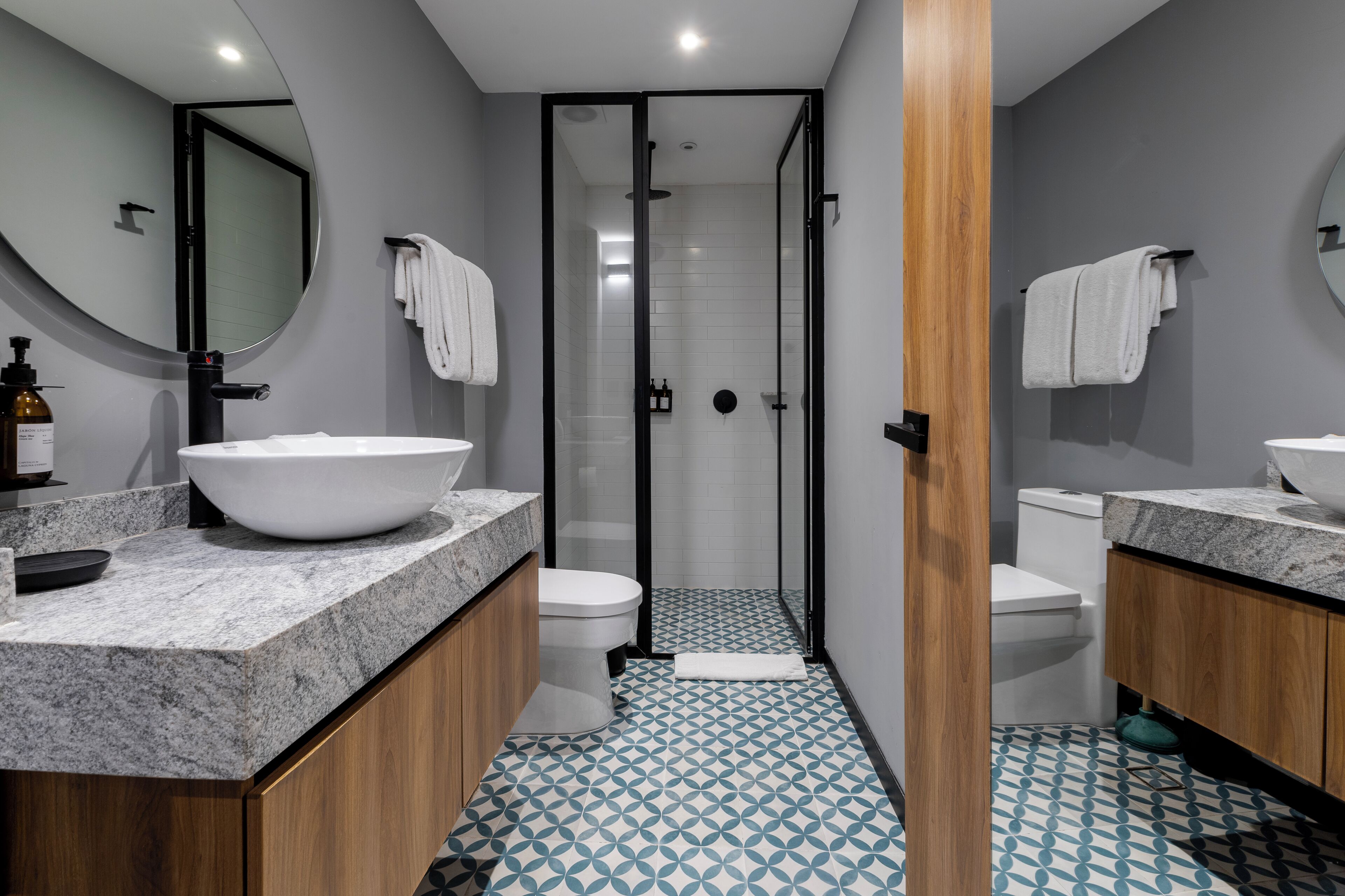 Un bagno moderno con un lavandino ovale grande, due servizi igienici, una doccia con pareti in vetro e piastrelle a motivi decorativi.