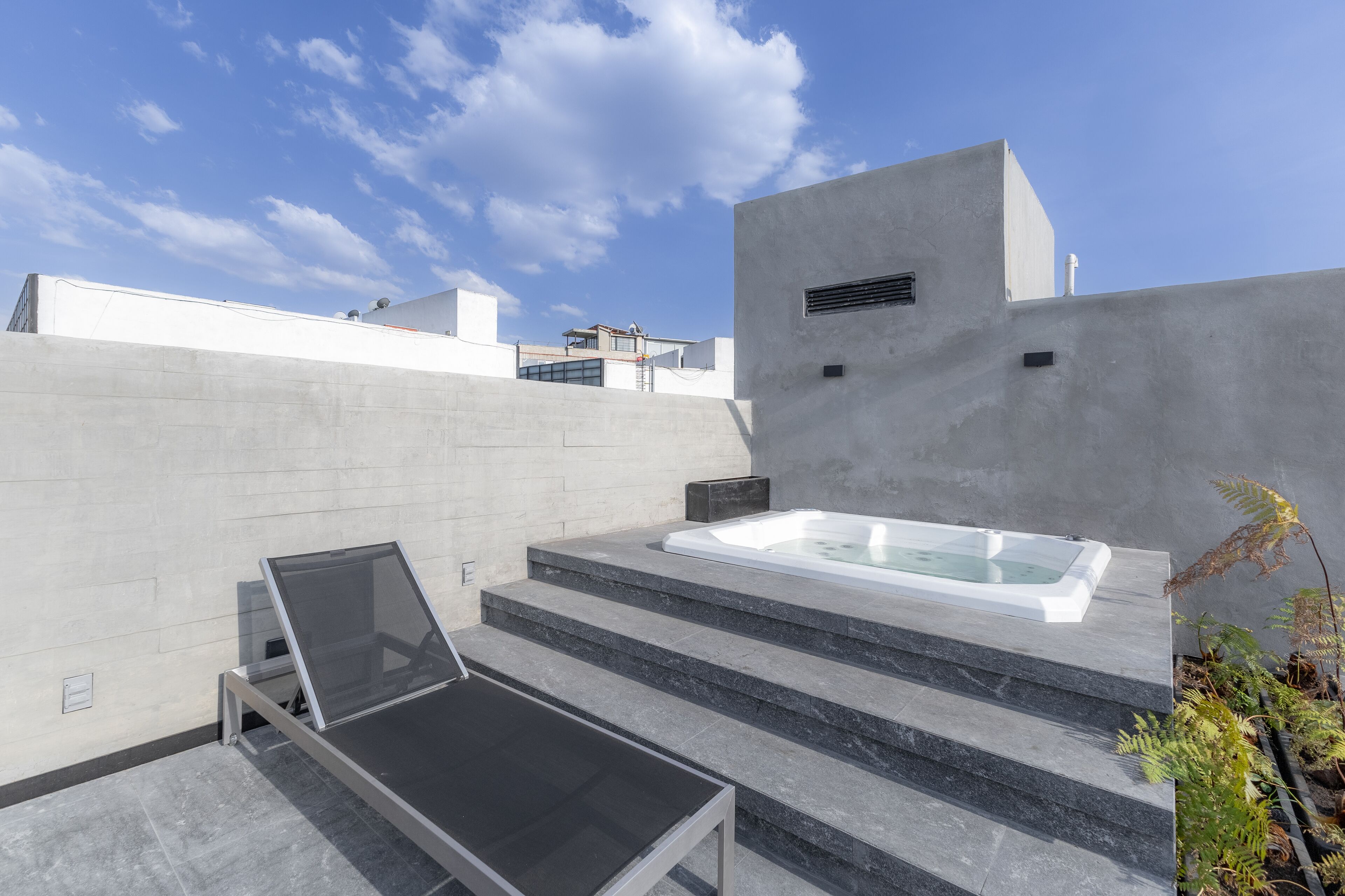 Ein moderner Außenbereich mit Spa-Bereich, Whirlpool, Liegestuhl und einer Treppe, die zu einer Dachterrasse führt.