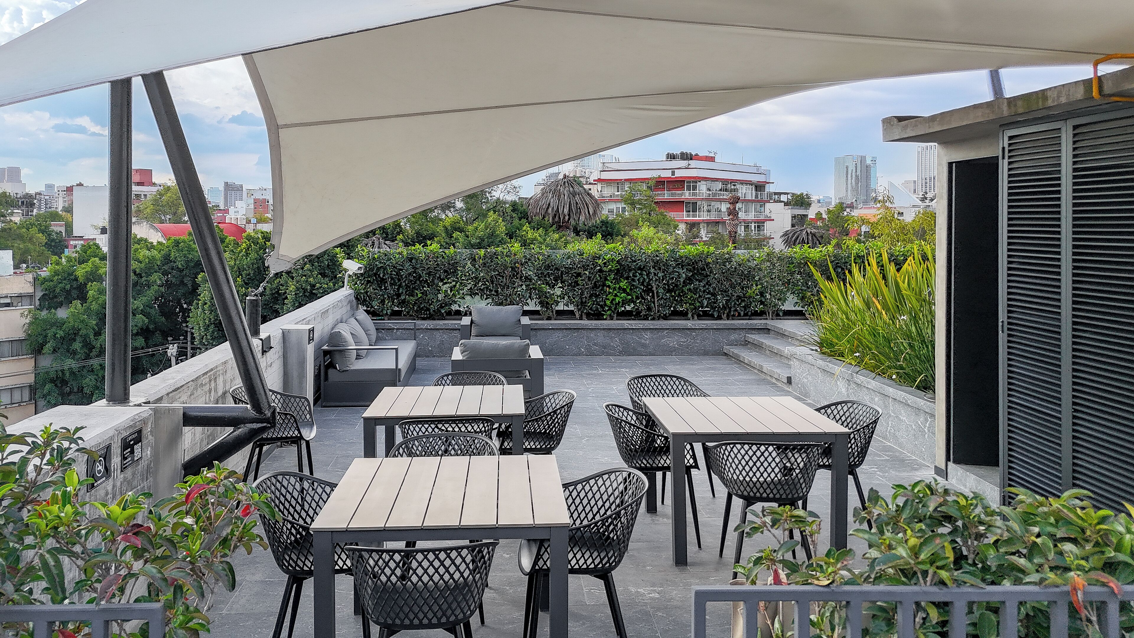 A rooftop patio with outdoor seating, including tables and chairs, and a large canopy providing shade.