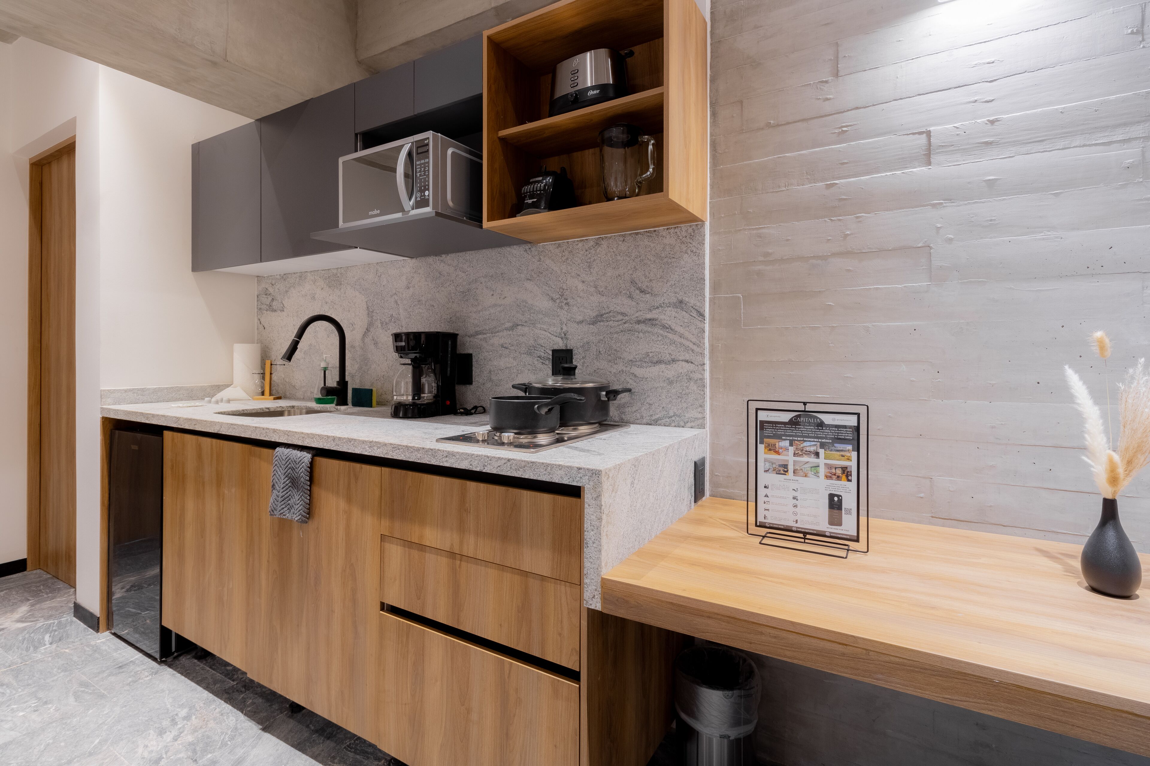 A modern kitchen with a built-in oven, microwave, and coffee maker. There is a wooden cabinet with a towel hanging on the handle.