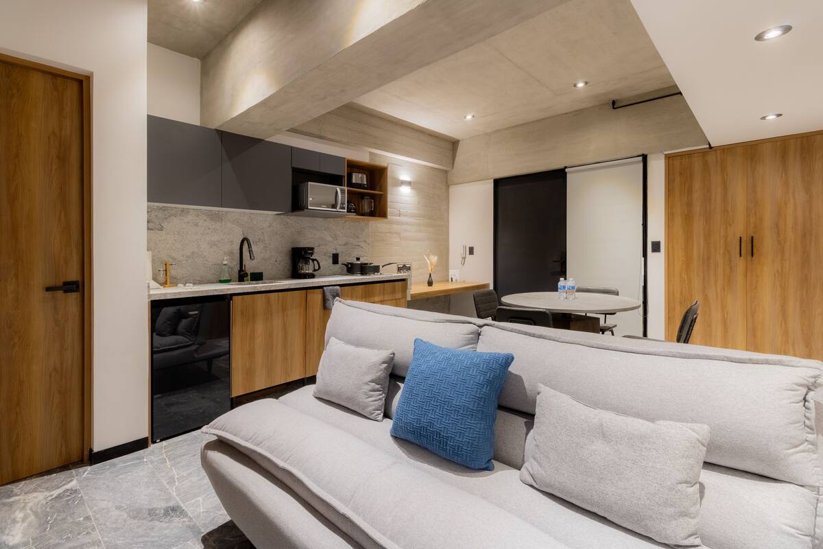 Una habitación de hotel moderna con sofá, kitchenette y mesa de comedor.