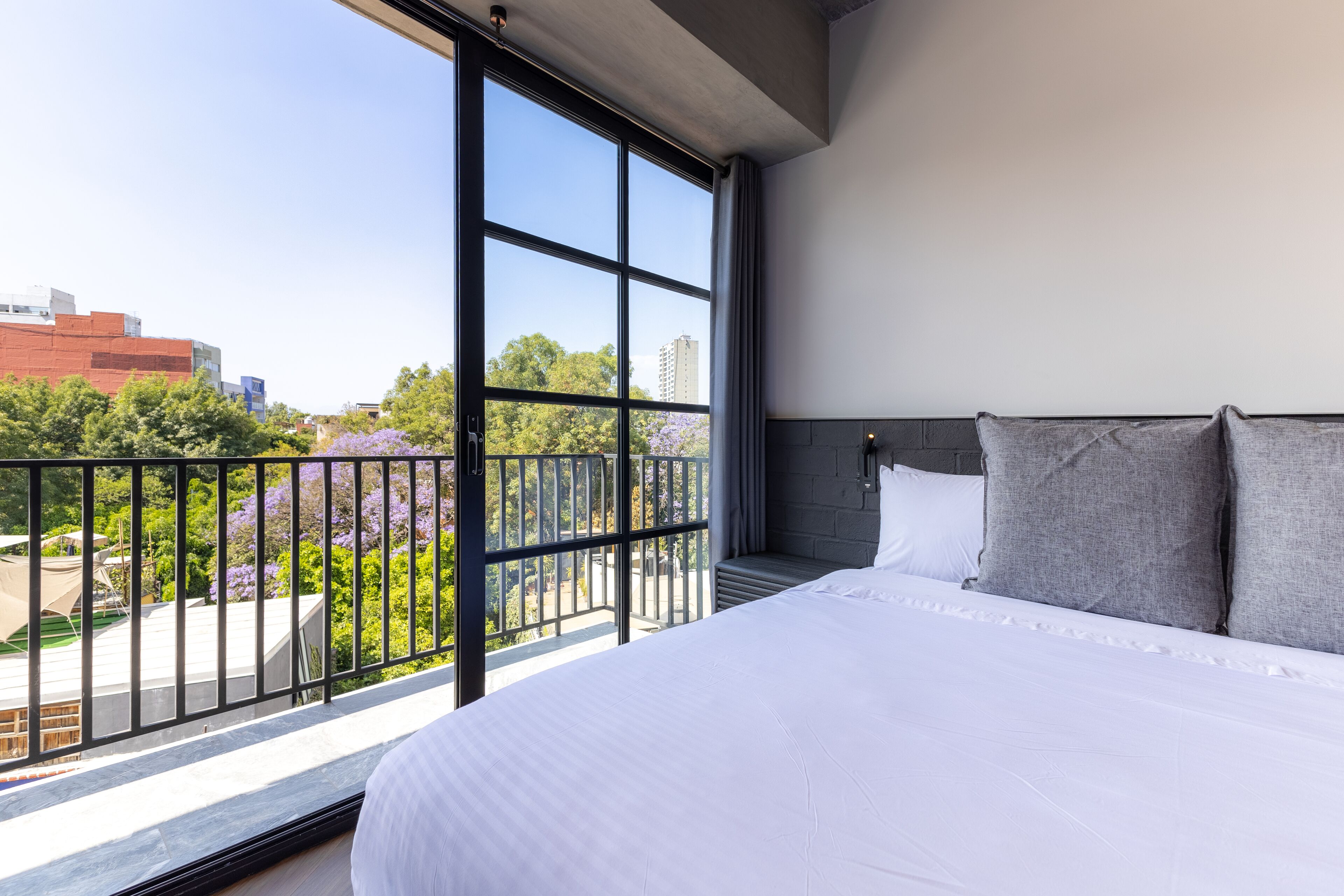 A modern hotel room with a large bed, a balcony with a view of the city, and a large window.