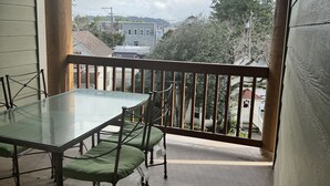 Ein Balkon mit Glastisch und Stühlen, Blick auf Gebäude und Bäume, und Holzgeländer.