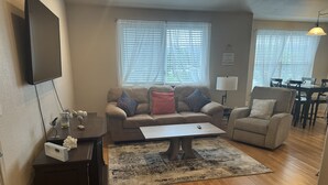 Ein Wohnzimmer mit Sofa, Sessel, Couchtisch und einem Essbereich im Hintergrund.