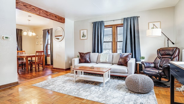 Een woonkamer met een bank, salontafel, voetenbankje, lederen fauteuil en een eethoek met stoelen en een tafel.