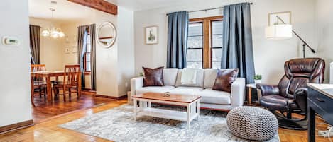 A living room with a sofa, coffee table, ottoman, leather chair, and a dining area with chairs and a table.