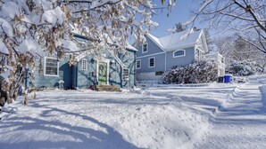Een huis met twee verdiepingen, een besneeuwde voortuin en een helderblauwe lucht.