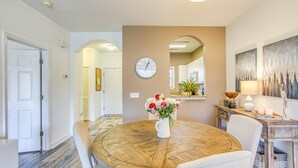 A dining area with a round wooden table, white chairs, a clock on the wall, and a vase of flowers. - Swim, Golf & Unwind: Barefoot Resort Condo (North Myrtle Beach)