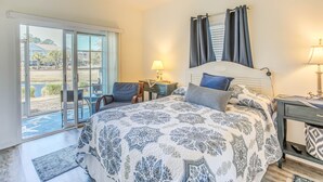 A bedroom with a large bed, a desk, a chair, and a view of the outdoors through a sliding door. - Swim, Golf & Unwind: Barefoot Resort Condo (North Myrtle Beach)