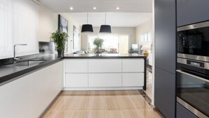 Une cuisine moderne dotée d’un îlot central, d’appareils électroménagers en acier inoxydable et de luminaires suspendus.