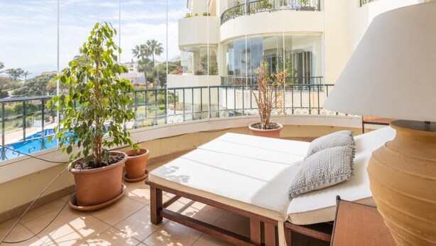 Un balcon avec vue sur la piscine, une chaise longue et des plantes en pot.