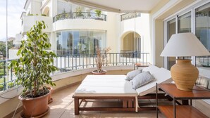 Un balcon avec un lit, une plante en pot et une table avec une lampe.