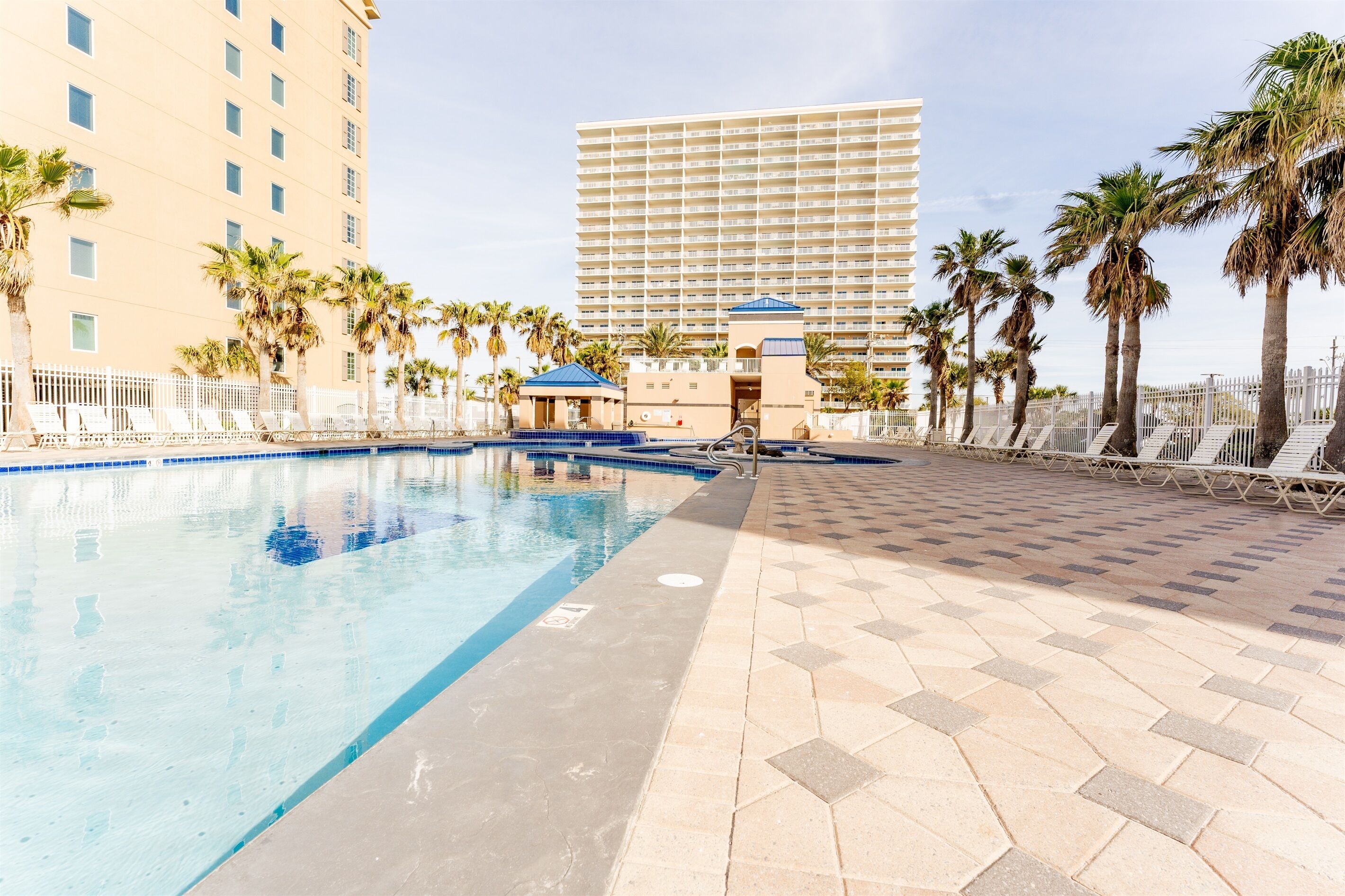 A swimming pool with lounge chairs and palm trees, surrounded by a high-rise building.
