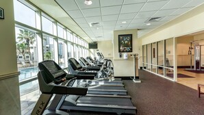 A gym with treadmills aligned along a wall with large windows. - 3 Pools - Skywalk- 2 Bedroom Updated Condo - Free Daily Activities! (Gulf Shores)