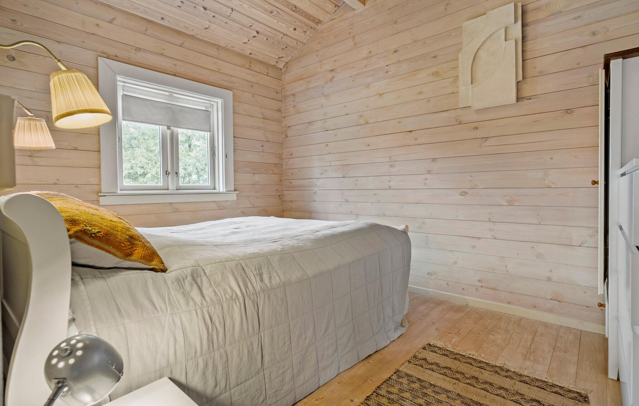 A bedroom with a bed, a window, a lamp, and a door.