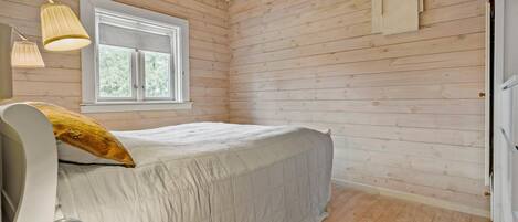 A bedroom with a bed, a window, a lamp, and a door.