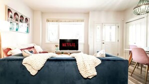 A living room with a dark blue sofa, a television displaying 'NETFLIX', and a chandelier. - ☆Mediterranean Retreat☆King Bed★Fireplace★Garage (Edmonton)