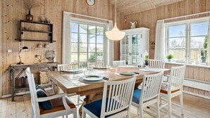 Ein Esszimmer mit Holzwandverkleidung, einem großen Tisch für sechs Personen, weißen Stühlen und einer hängenden Leuchte.