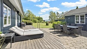 Eine Terrasse mit Gartenmöbeln, ein Rasen und Blick aufs Wasser.
