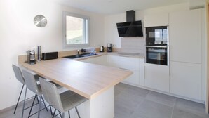 A modern kitchen with a central island, built-in oven, and a window providing natural light. - Pretty new and comfortable house between towns and lakes (Voglans)