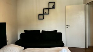 A bedroom with a bed, a door, and a wall-mounted shelf with items.
