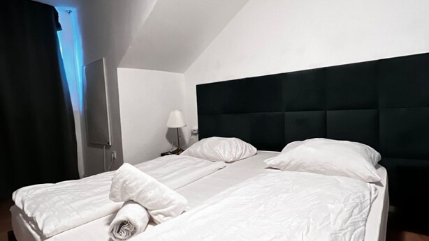 A hotel room with a bed, a nightstand, a lamp, and a wall-mounted TV.