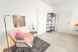 A modern living room with a pink sofa, a small round table, a potted plant, a floor lamp, and a black shelving unit.
