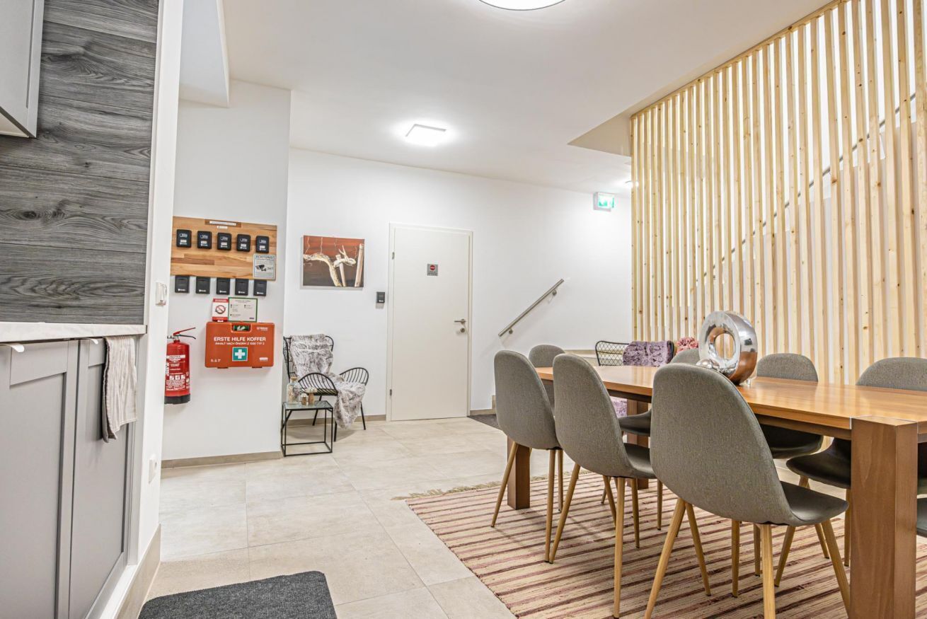 Een moderne eetruimte met een houten tafel en stoelen, een brandblusser en rookmelder aan de muur.