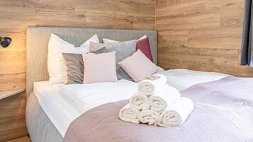 Una cama bien hecha con toallas enrolladas, una lámpara de noche y un cabecero de madera.