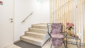 A staircase with a handrail, a chair with a fluffy blanket, and a small table with a vase of flowers.