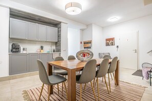 A modern kitchen with grey cabinets, a wooden dining table with six chairs, and a kitchen island with a coffee machine.