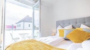 A bedroom with a bed, pillows, a bedside table, and a view through a glass door.